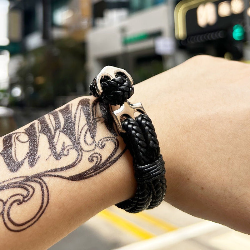 Bracelet tressé noir pour homme avec fermoir ancre argentée sur poignet tatoué.