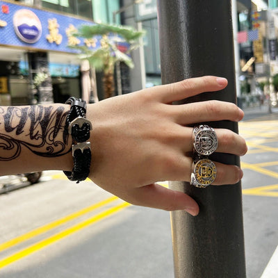 Bracelet tressé noir avec ancre métallique porté au poignet masculin tatoué, en ville.
