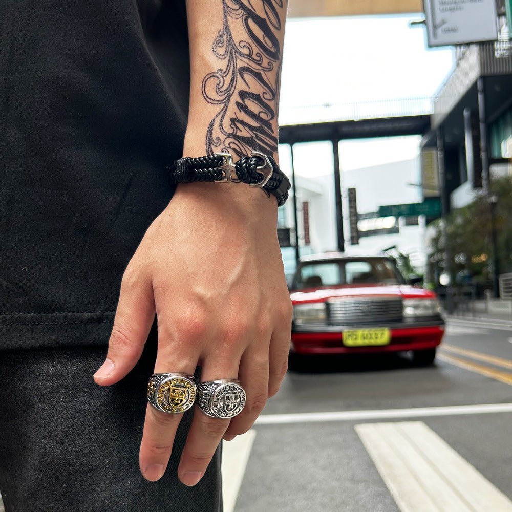 Bracelet tressé noir avec ancre métallique argentée porté au poignet d’un homme tatoué.
