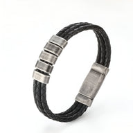 Bracelet triple cordon cuir noir tressé avec trois plaques métalliques argentées et fermoir aimanté.