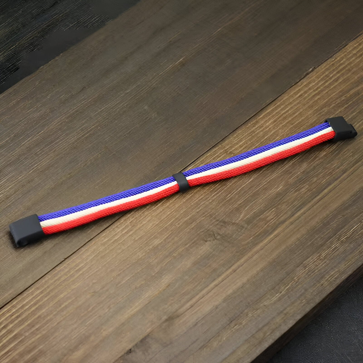 Bracelet triple cordons bleu, blanc, rouge pour homme avec fermoir noir posé sur table en bois.