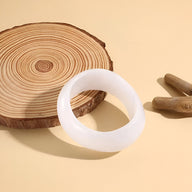 Bracelet large en acrylique blanc translucide au design lisse et épuré posé sur un fond beige clair.