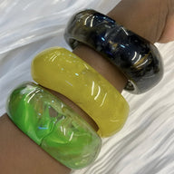 Trois bracelets épais en acrylique lisse, jaune vif, vert translucide et noir marbré, style Thalina.