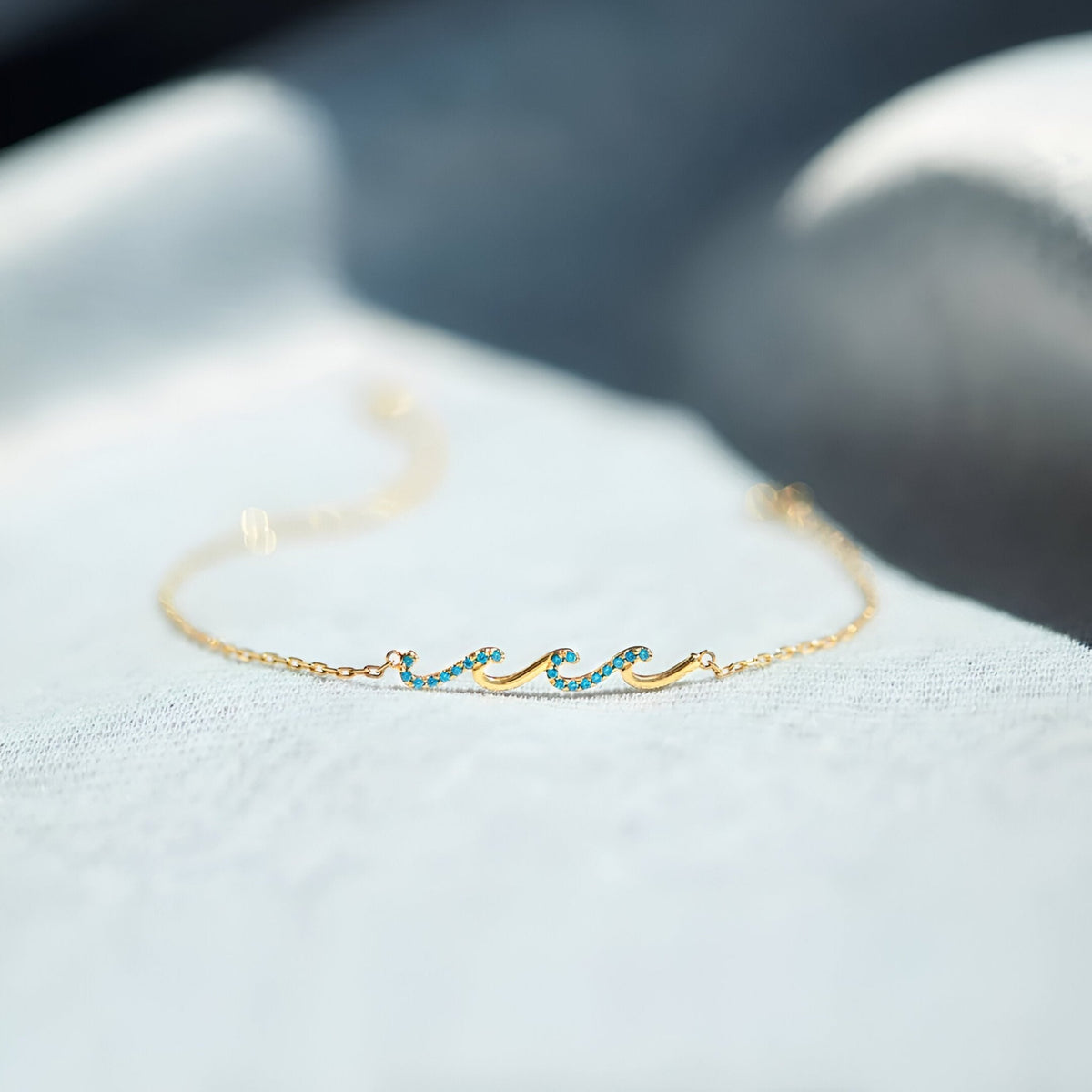 Bracelet fin en or avec motif vague en émail turquoise et chaîne délicate.