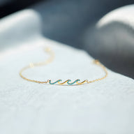 Bracelet fin en or avec motif vague en émail turquoise et chaîne délicate.