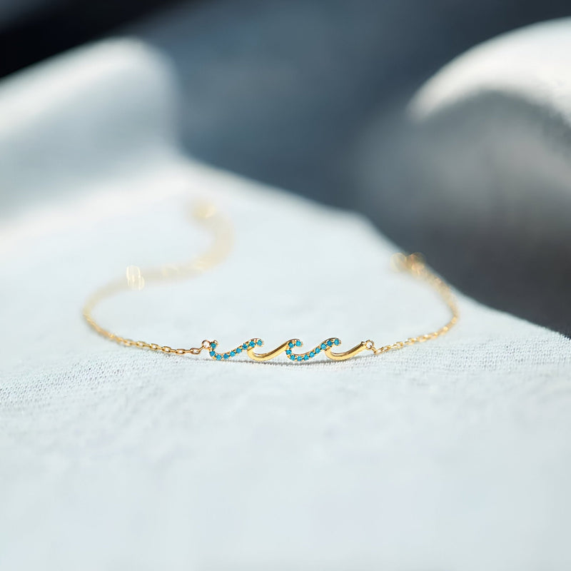 Bracelet fin en or avec motif vague en émail turquoise et chaîne délicate.