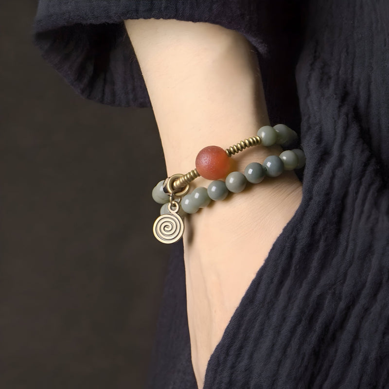 Bracelet femme en graines de Bodhi et perles d'agate gris avec breloque spirale dorée.