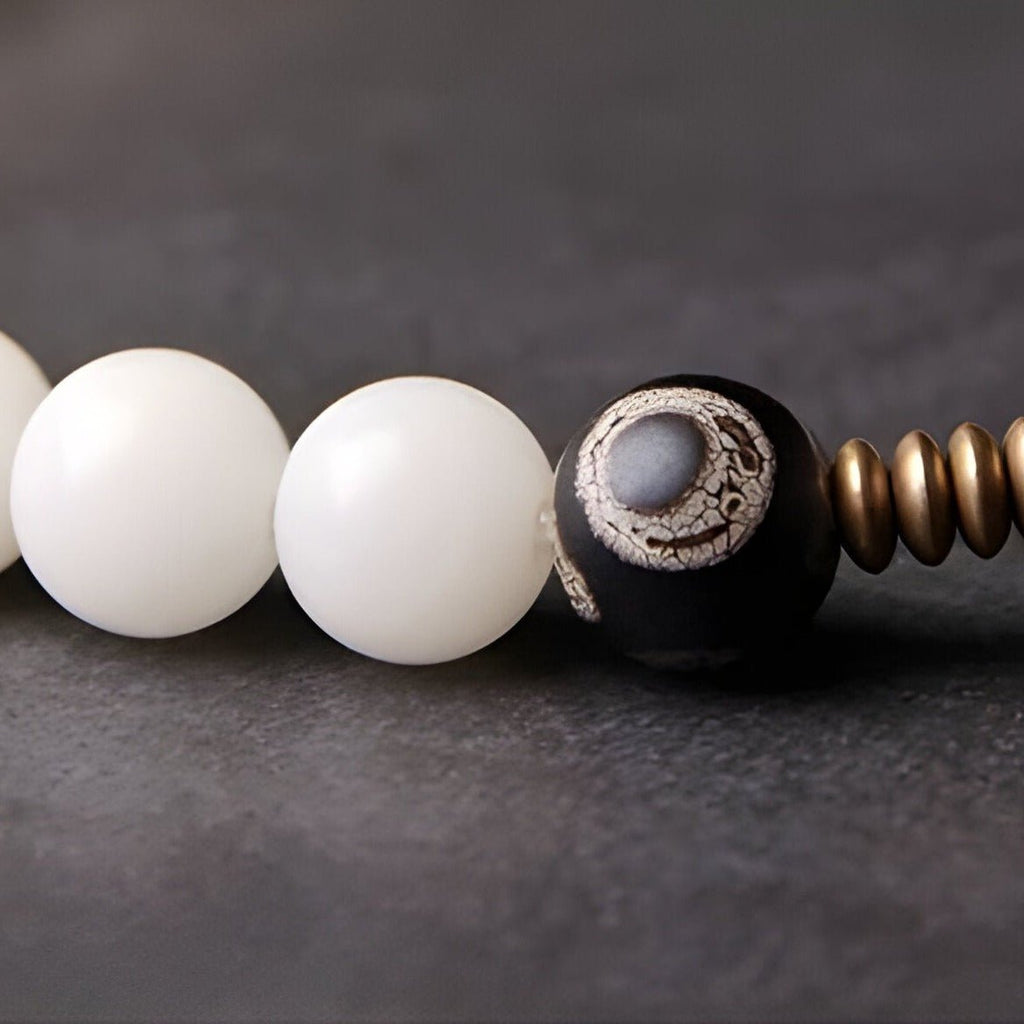 Bracelet femme avec perles rondes blanches en pierre d'agate et perle noire Bodhi motif naturel sur fond gris.