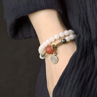 Bracelet en pierres d'agate blanches, perle orange en graines de Bodhi, pendentif spirale métallique, porté au poignet.