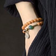 Bracelet en graines de Bodhi orange avec perle d'agate verte et pendentif spirale en métal argenté.