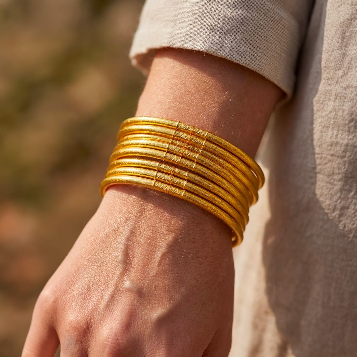 Lot de neuf bracelets joncs dorés en silicone souple, design minimaliste et empilable, porté au poignet.