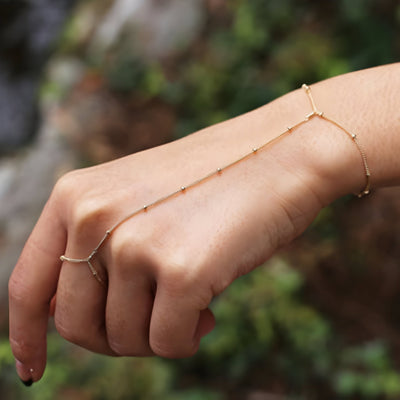 Bijou de main en acier inoxydable doré avec petites perles, chaîne fine reliant doigt et poignet.