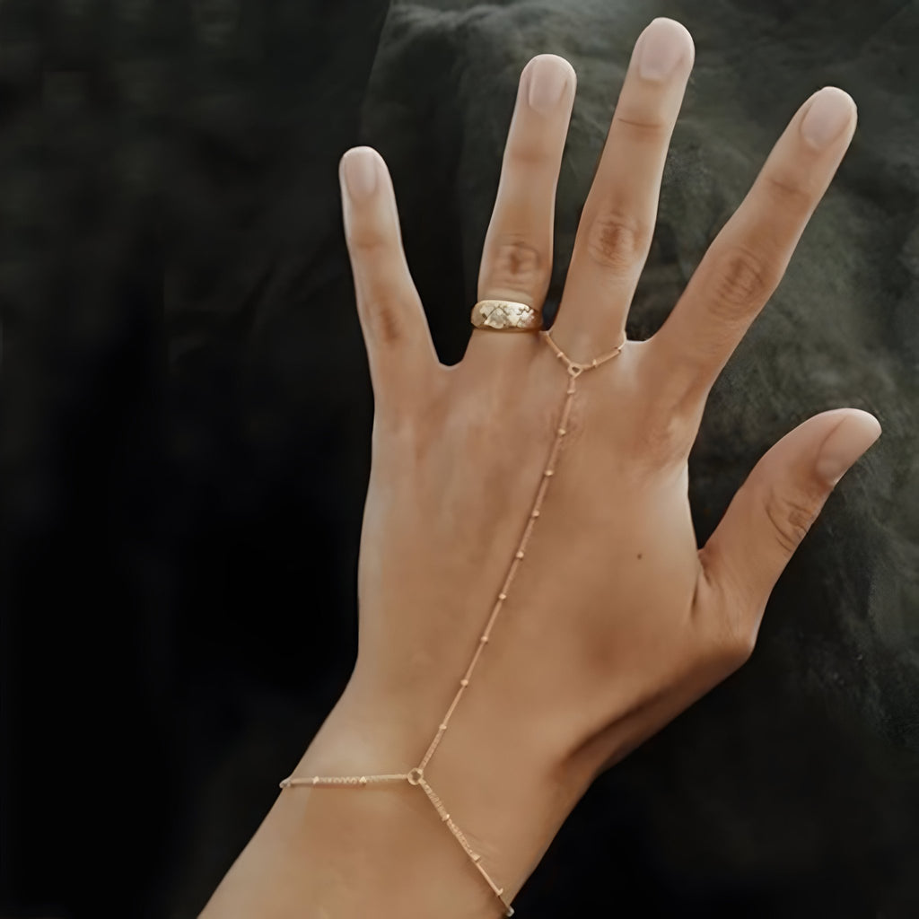 Bijou de main en acier inoxydable doré avec perles fines et chaîne élégante reliant bague et bracelet.