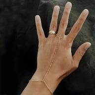 Bijou de main en acier inoxydable doré avec perles fines et chaîne élégante reliant bague et bracelet.