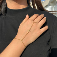 Bijou de main en acier inoxydable doré avec croix chrétienne et chaîne fine portée au doigt et au poignet.