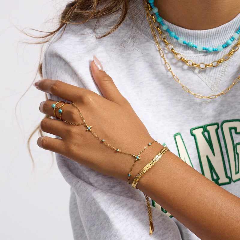 Chaîne de doigt dorée en acier inoxydable avec perles turquoise et petite croix chrétienne, portée au doigt et au poignet.