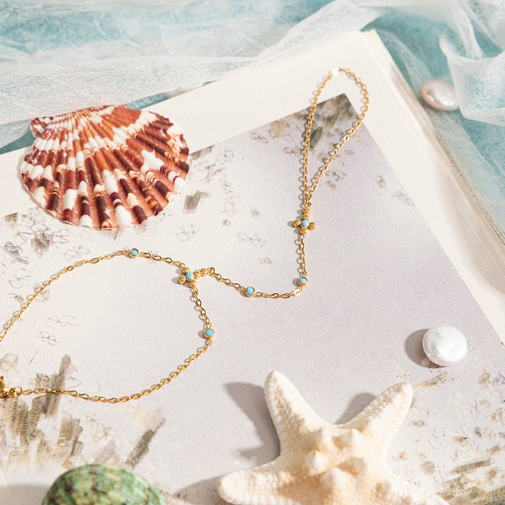 Chaîne de doigt dorée en acier inoxydable avec perles turquoise et petite croix chrétienne délicate.