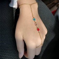 Bijou de main doré avec chaîne fine et trois zirconiums bleu, blanc et rouge sur dos de main féminine.