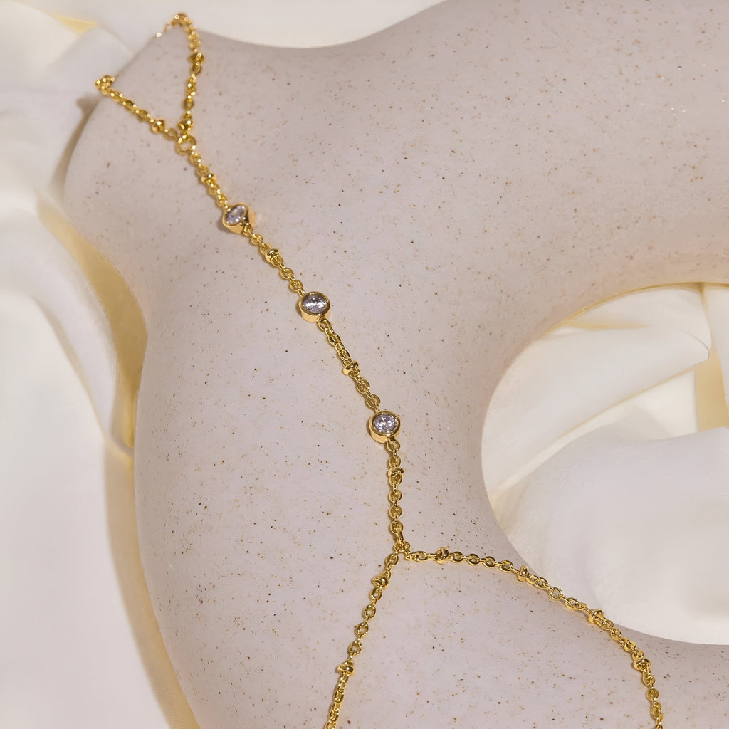 Bijou de main en acier inoxydable doré avec zirconiums, chaîne fine reliant doigt et poignet.