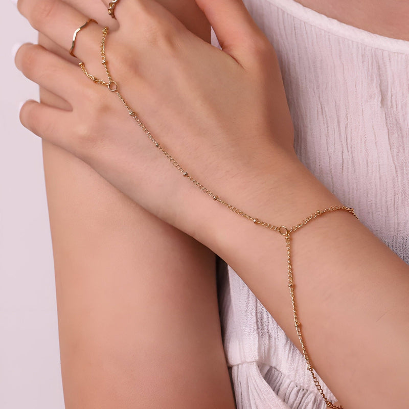 Bijou de main en acier inoxydable doré, chaîne fine reliant un anneau à un bracelet ajustable.