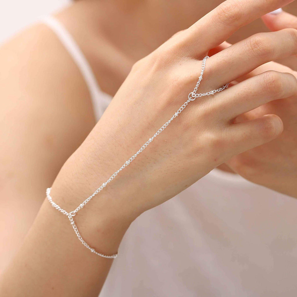 Bijou de main en acier inoxydable argenté avec chaîne fine reliant un bracelet à une bague minimaliste.