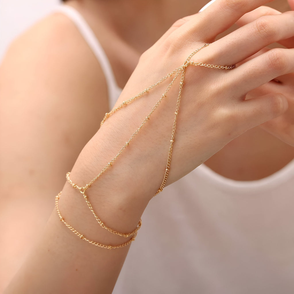 Bijou de main multi-rangs en acier inoxydable doré, chaînes fines élégantes entourant le poignet et le doigt.