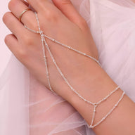 Bijou de main multi-rangs en acier inoxydable argenté avec chaînes fines reliant bague et bracelet.