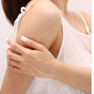 Bijou de main multi-rangs en acier inoxydable doré avec délicates chaînes fines et petites perles sur peau femme en tenue.