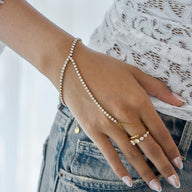 Chaîne de main dorée en métal fin avec zircon scintillant reliant poignet et doigt, style délicat et élégant.