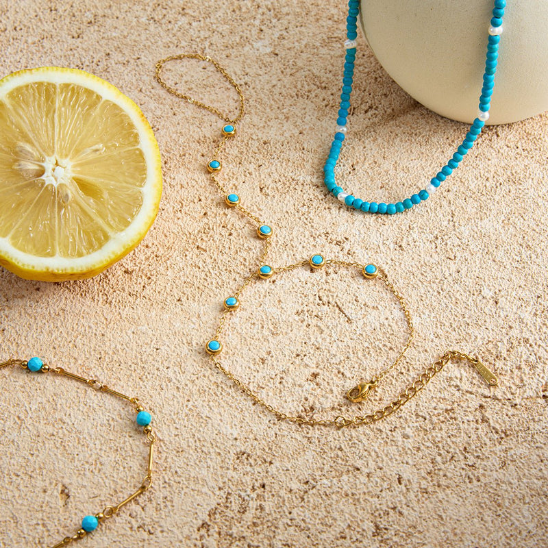 Chaînette de main dorée en acier inoxydable avec petites pierres turquoise rondes, finition brillante.