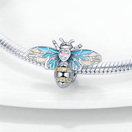 Charm abeille argentée avec ailes bleues et cœur en cristal transparent, détails jaunes sur le corps.