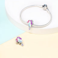 Charm pendentif aile de papillon argenté avec détails roses et bleus, sur bracelet serpent argenté.