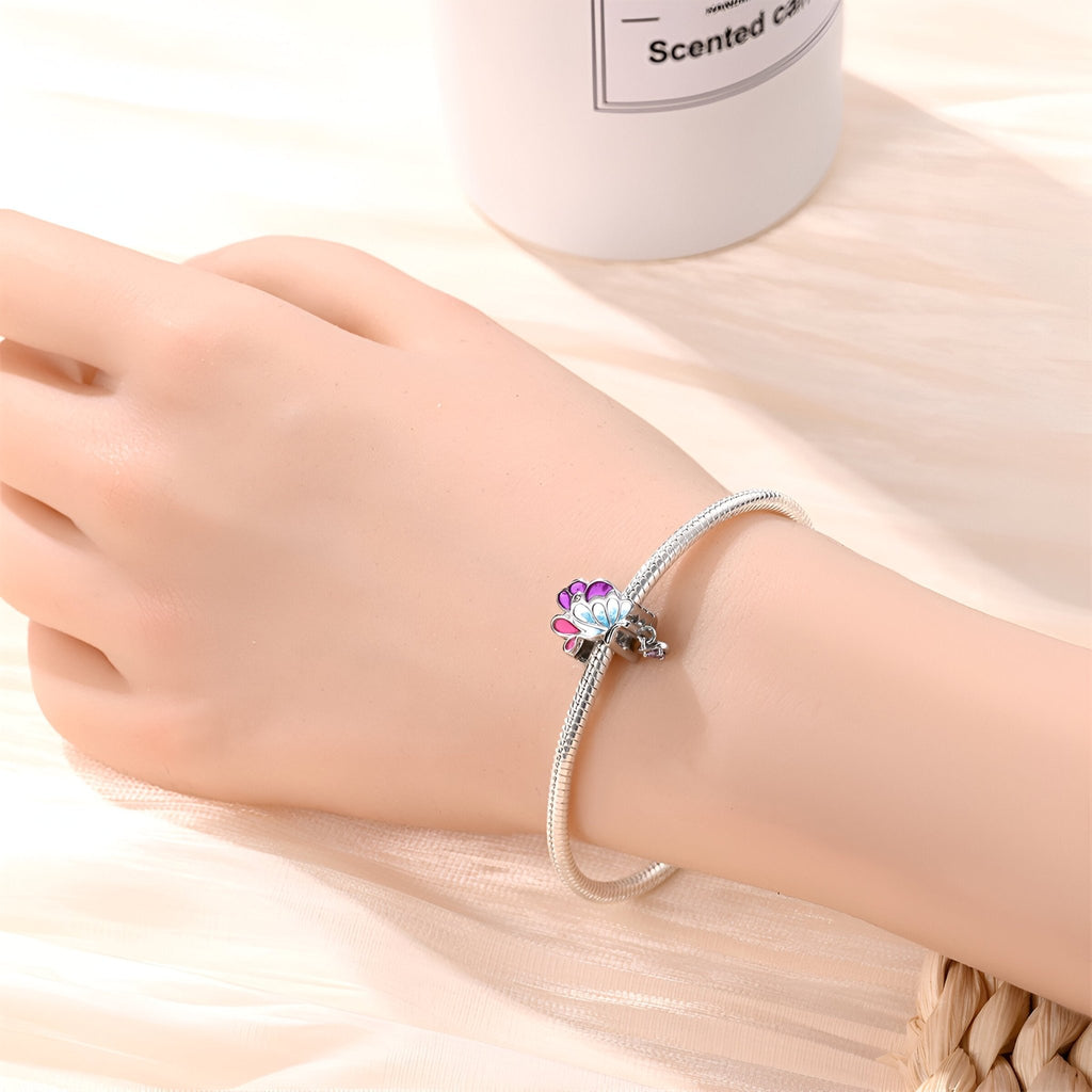 Bracelet argenté avec charm en forme d'aile de papillon rose et violet.