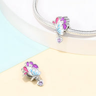 Charm aile de papillon en argent avec émail rose, bleu, violet et pendentif cœur violet.