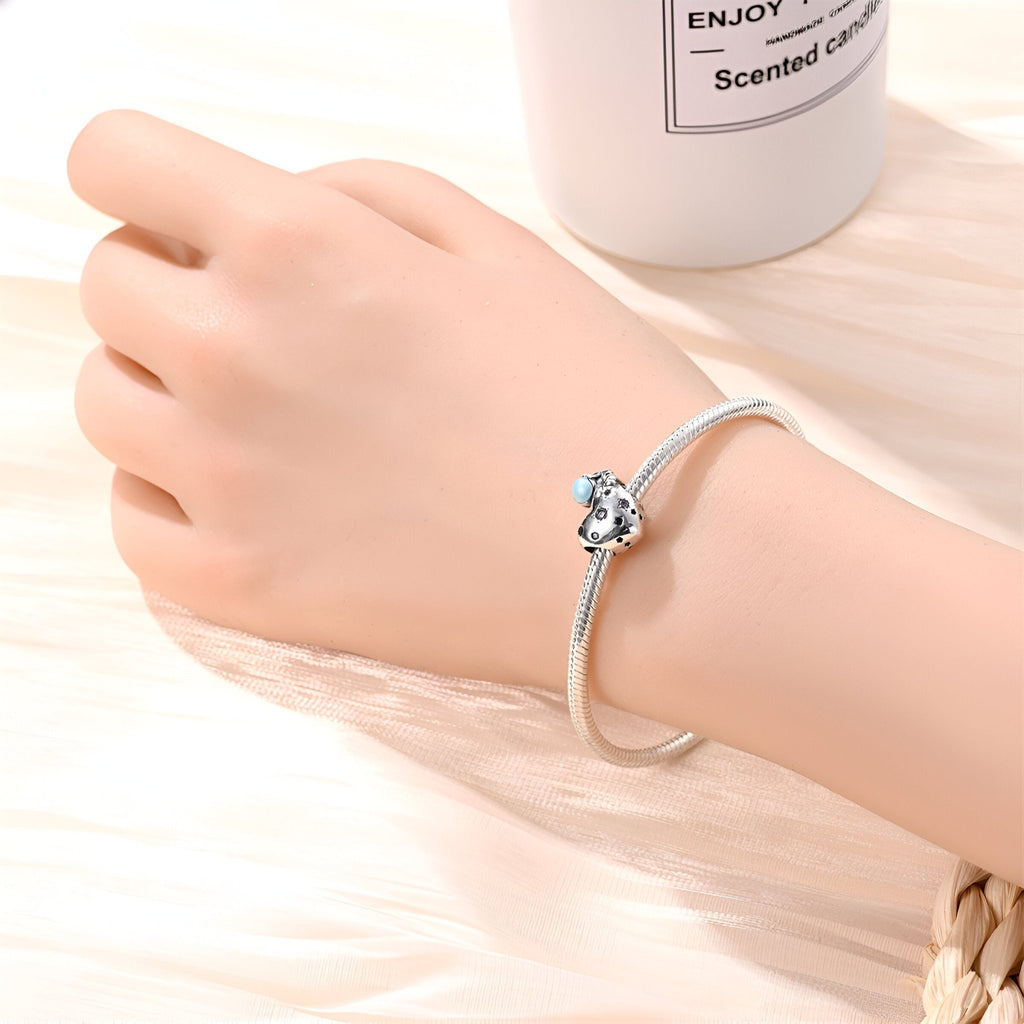 Bracelet argenté avec charm astronaute sur un cœur brillant porté au poignet.
