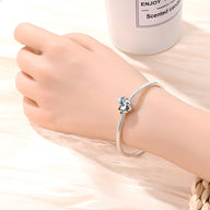 Bracelet argenté avec charm astronaute sur un cœur brillant porté au poignet.