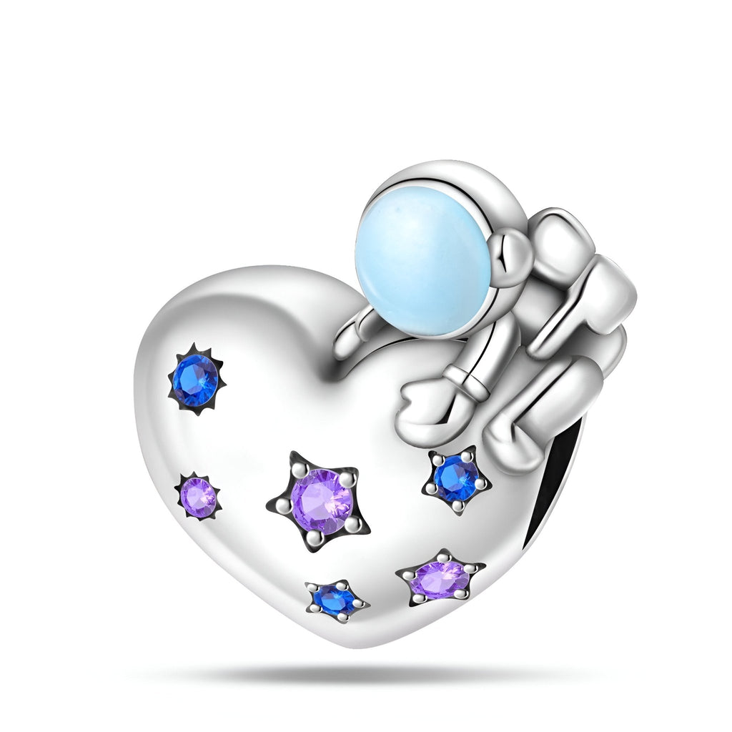 Charm argenté en forme de cœur avec astronaute et pierres bleues et violettes scintillantes.