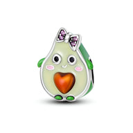 Charm avocat vert pâle avec cœur orange, yeux expressifs et nœud papillon violet en strass.