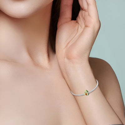 Bracelet fin en corde blanche avec charm avocat vert et noyau en forme de cœur doré.
