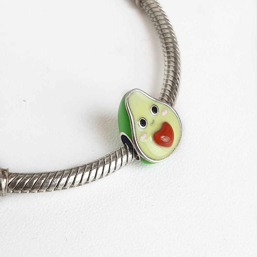 Charm en forme d'avocat vert avec noyau cœur rouge en émail sur bracelet argenté.