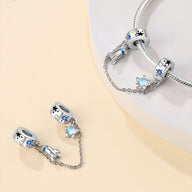 Charm en argent avec fusée spatiale et étoile bleue, chaînette de sécurité fine, style contemporain.