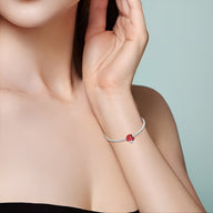 Bracelet fin argenté avec charm champignon rouge à pois blancs porté au poignet féminin.