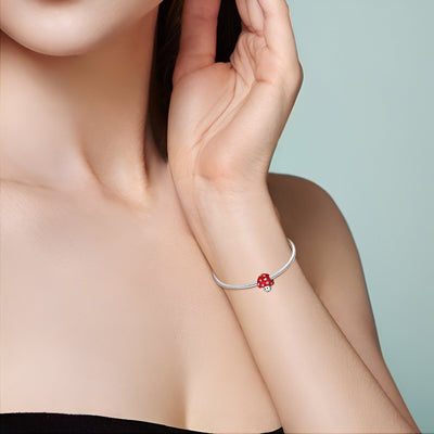 Bracelet fin argenté avec charm champignon rouge à pois blancs porté au poignet féminin.