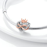 Charm en forme de cœur argenté texturé avec un signe infini et une couronne rose en métal sur un bracelet serpent argenté.