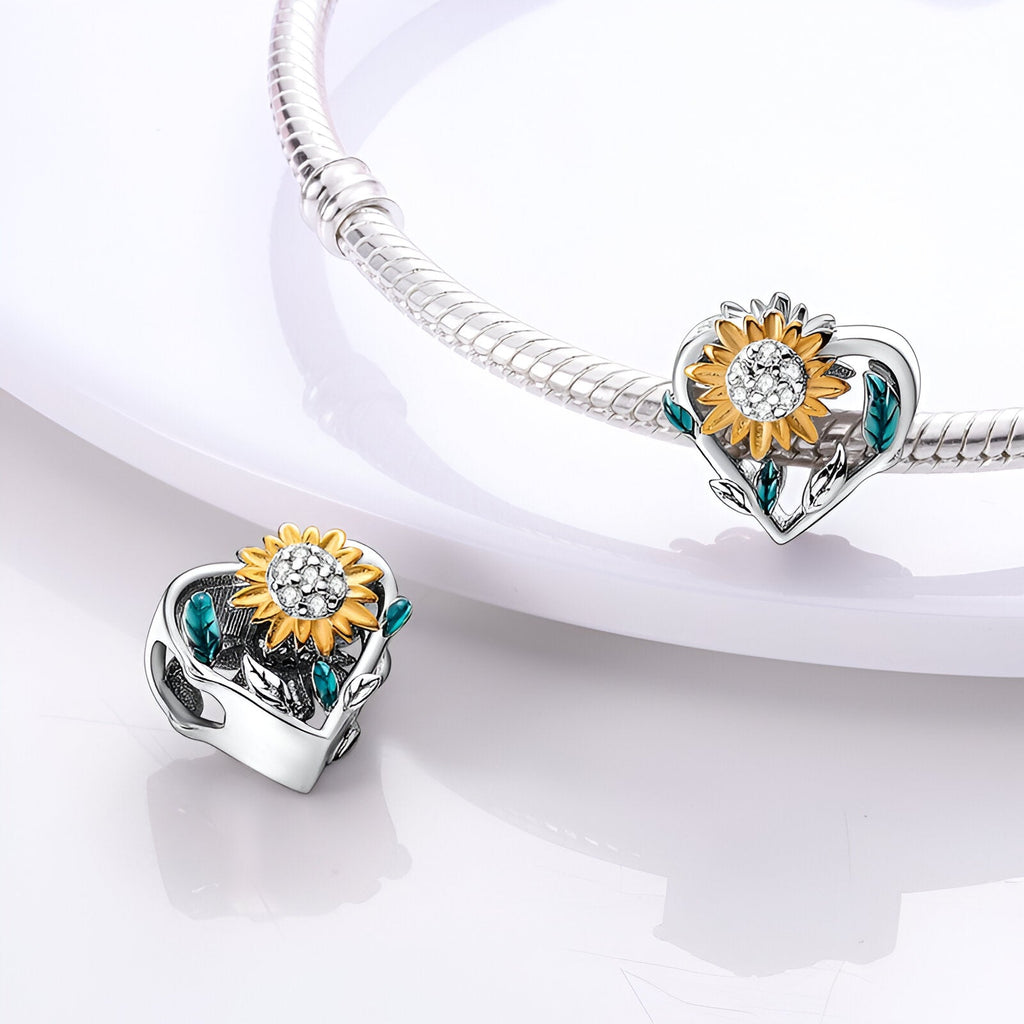 Charm en forme de cœur argenté orné d'un tournesol jaune et de feuilles vertes sur bracelet serpent.
