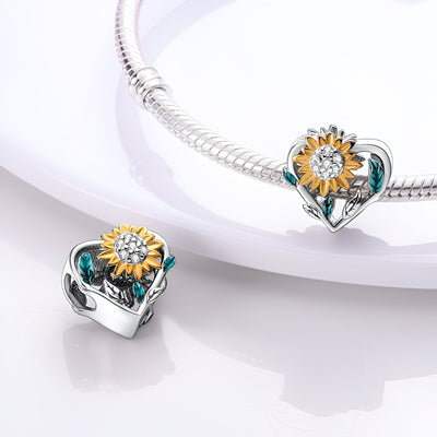 Charm en forme de cœur argenté orné d'un tournesol jaune et de feuilles vertes sur bracelet serpent.