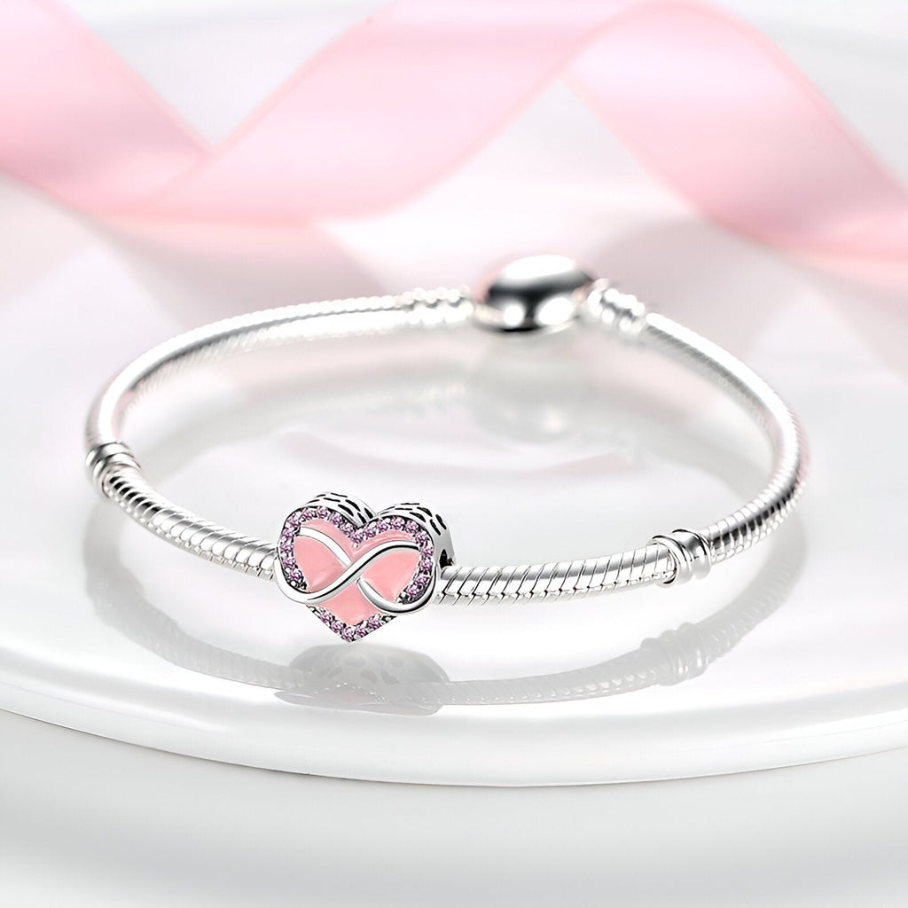 Bracelet argent avec charm cœur rose et symbole infini au centre, design élégant et fin.