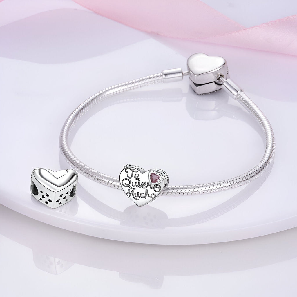 Bracelet argenté avec charme cœur gravé "Te quiero mucho" orné d'une petite pierre rose et un autre charm carré avec motif.