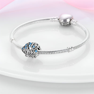 Bracelet argenté avec charm coquillage ajouré orné de perles et étoiles bleues.