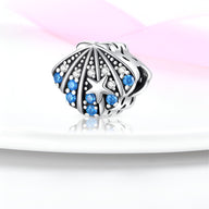 Charm coquillage en argent orné de petites perles blanches et strass bleu ciel.